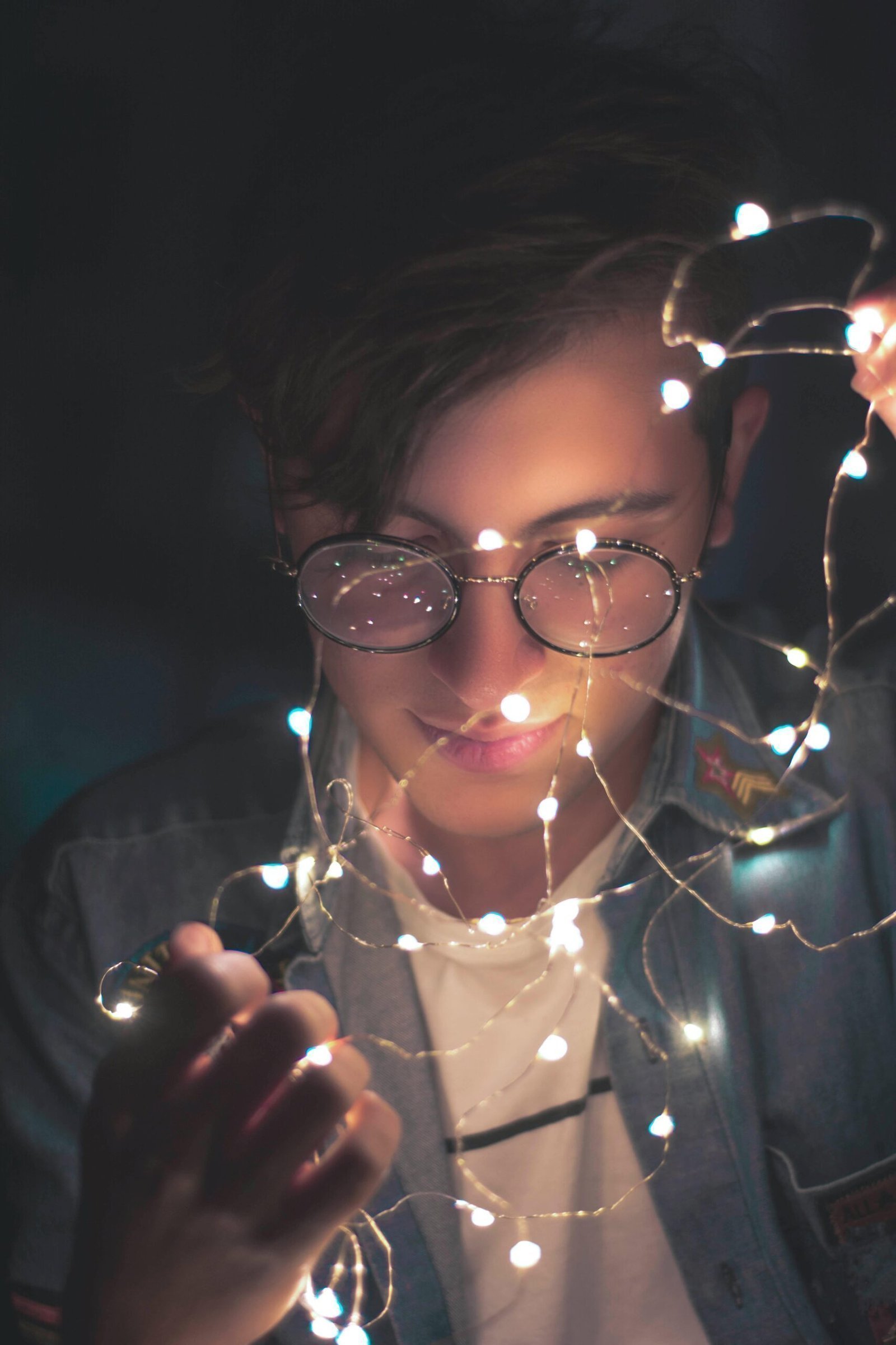 Young man with glasses illuminated by fairy lights, creating a stylish and artistic portrait.